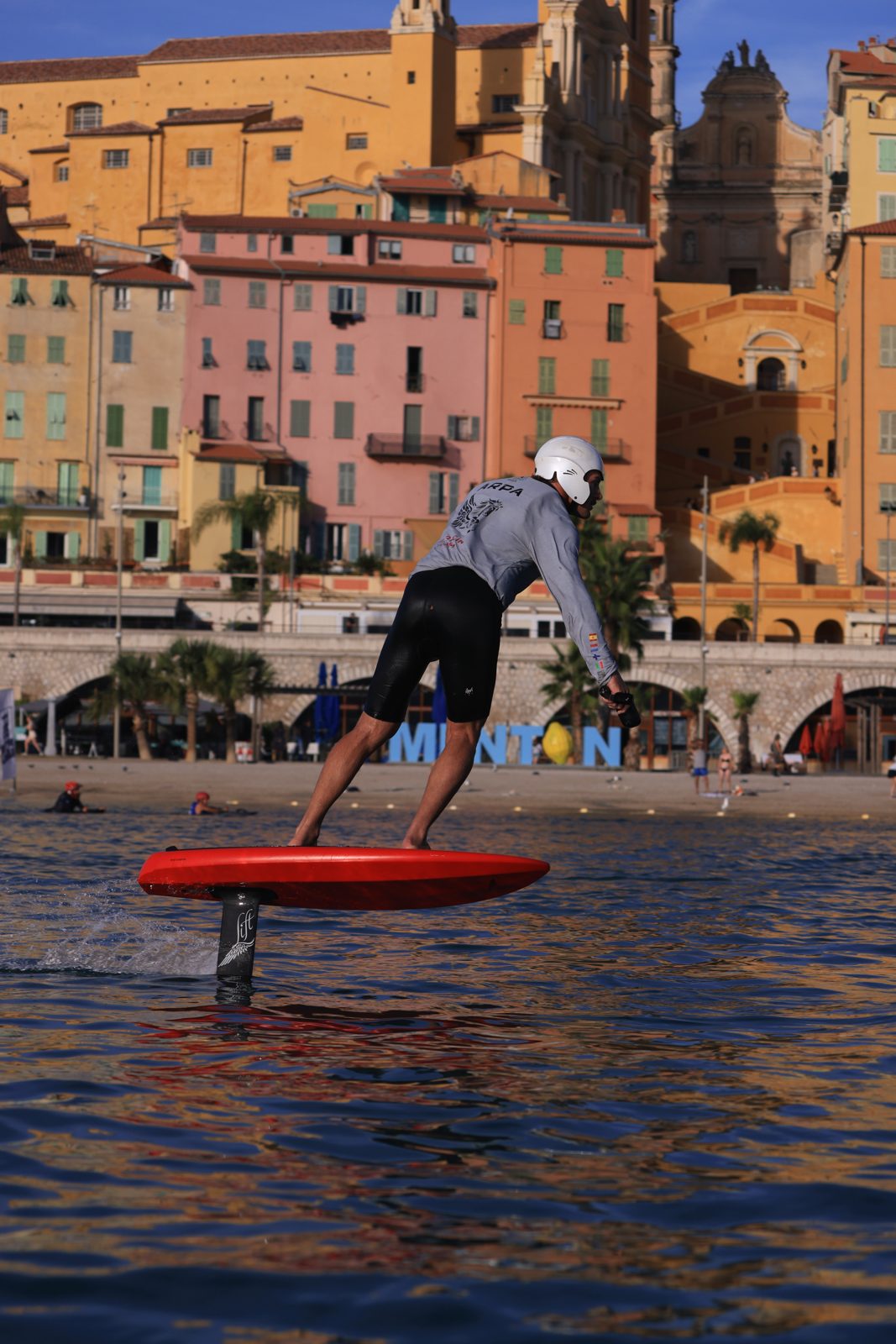Rider eFoil sur planche rouge devant les immeubles colorés de Menton